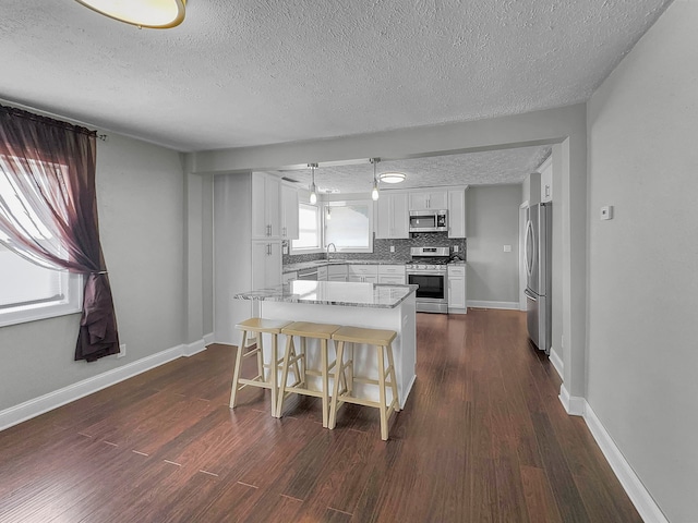 kitchen featuring white cabinets, a textured ceiling, appliances with stainless steel finishes, a center island, and a kitchen bar