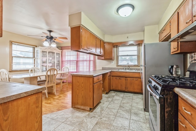 kitchen featuring ceiling fan, kitchen peninsula, stainless steel gas range oven, light wood-type flooring, and sink