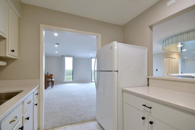 kitchen with light stone counters, white cabinets, white fridge, and light colored carpet