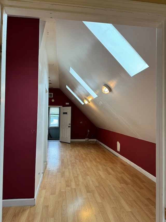 bonus room with vaulted ceiling with skylight and light hardwood / wood-style floors