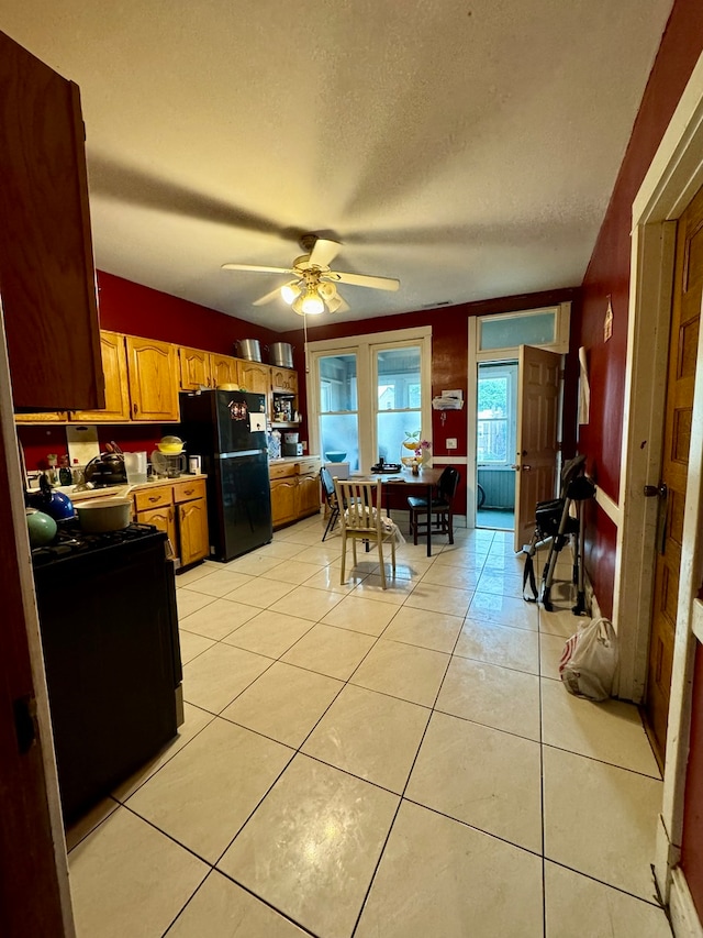 kitchen featuring a textured ceiling, light tile patterned floors, black fridge, and ceiling fan