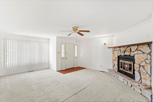 carpeted living room featuring a stone fireplace and ceiling fan