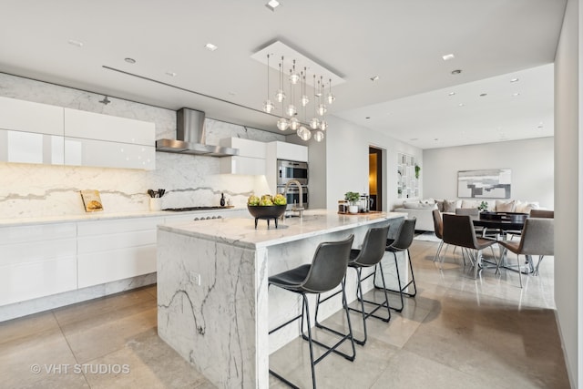 kitchen featuring a spacious island, white cabinetry, hanging light fixtures, and wall chimney range hood