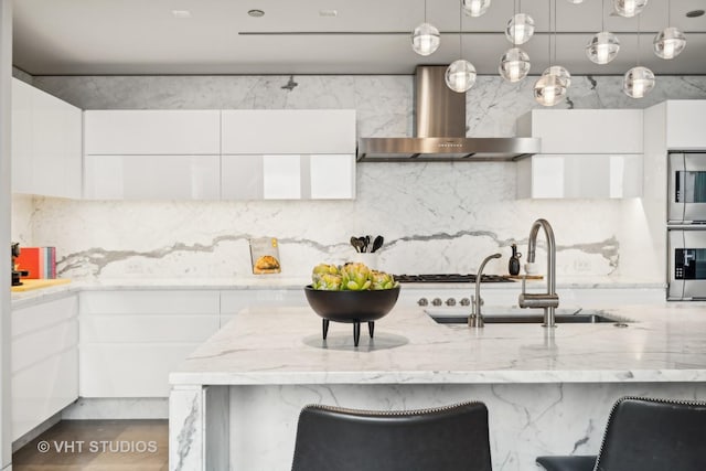 kitchen with wall chimney exhaust hood, modern cabinets, a sink, and white cabinetry