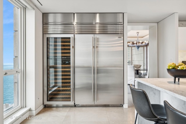 kitchen with a notable chandelier, light tile patterned flooring, built in fridge, and light stone countertops