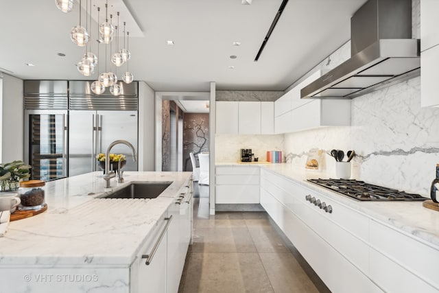 kitchen featuring hanging light fixtures, backsplash, sink, white cabinetry, and wall chimney exhaust hood