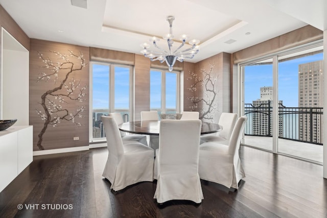 dining space with an inviting chandelier, a raised ceiling, and wood finished floors