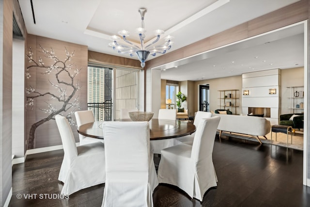 dining room featuring a notable chandelier, a large fireplace, dark hardwood / wood-style flooring, and a tray ceiling