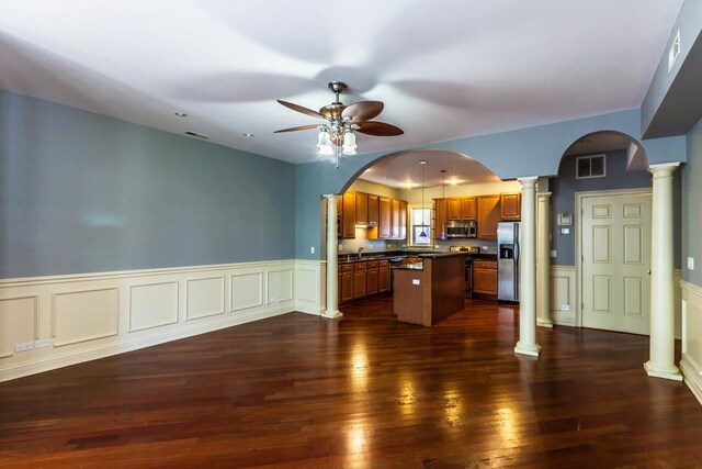 kitchen featuring decorative columns, dark hardwood / wood-style flooring, appliances with stainless steel finishes, a center island, and ceiling fan