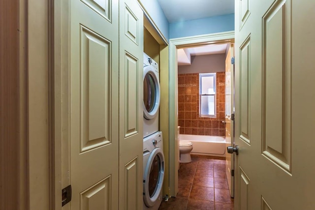 laundry room featuring stacked washer / dryer and dark tile patterned floors