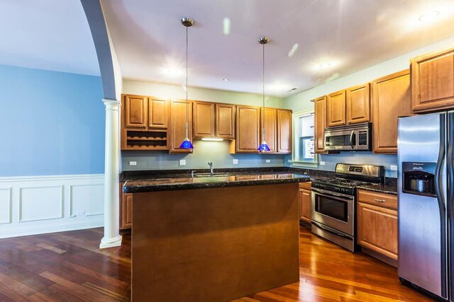 kitchen with dark hardwood / wood-style flooring, hanging light fixtures, appliances with stainless steel finishes, sink, and ornate columns