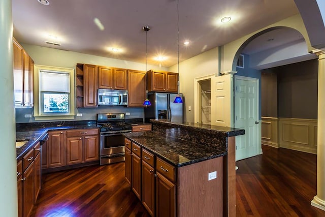 kitchen featuring hanging light fixtures, dark stone countertops, appliances with stainless steel finishes, a kitchen island, and decorative columns