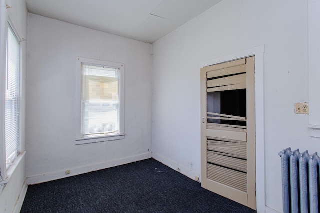 unfurnished room with radiator heating unit and dark carpet