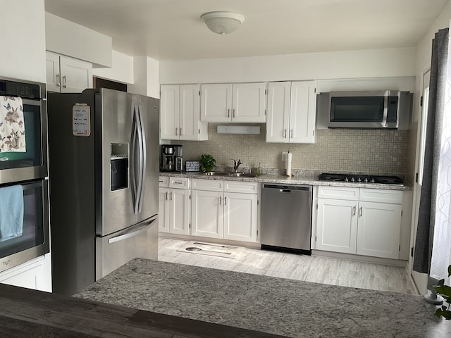 kitchen featuring backsplash, stainless steel appliances, white cabinetry, sink, and light wood-type flooring