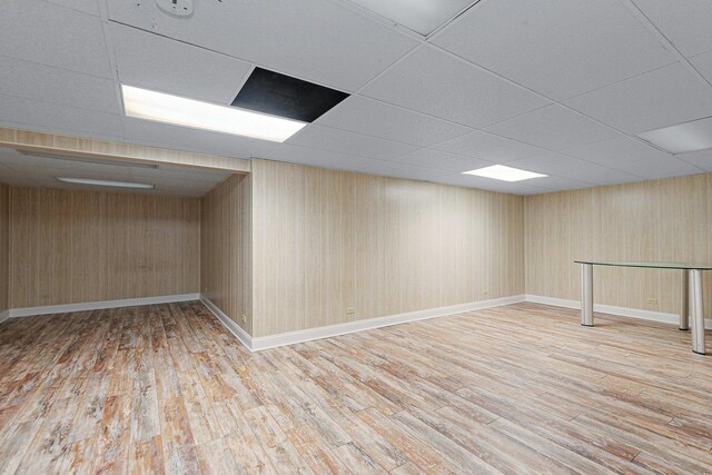 basement featuring wood walls, light wood-type flooring, and a drop ceiling