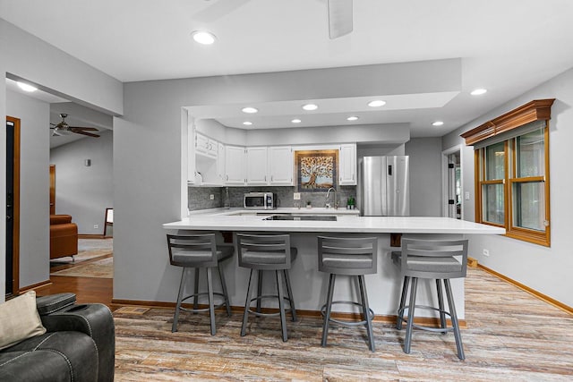 kitchen with a breakfast bar area, white cabinets, kitchen peninsula, stainless steel appliances, and light hardwood / wood-style flooring