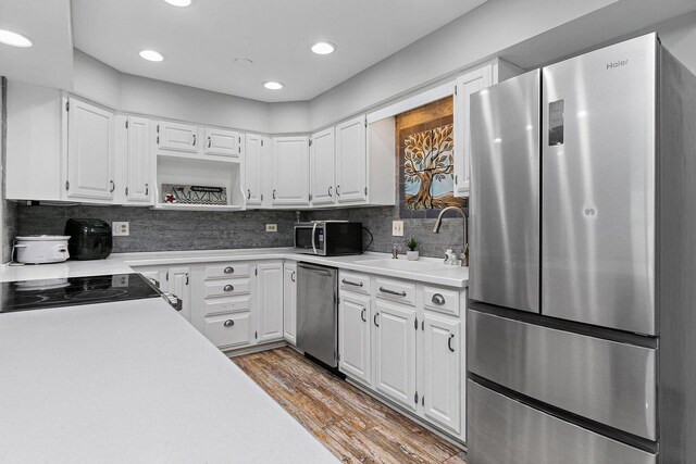 kitchen with tasteful backsplash, stainless steel appliances, white cabinetry, light hardwood / wood-style flooring, and sink