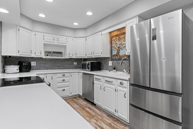 kitchen featuring sink, appliances with stainless steel finishes, hardwood / wood-style floors, decorative backsplash, and white cabinets