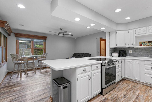 kitchen featuring ceiling fan, backsplash, stainless steel range with electric cooktop, light hardwood / wood-style flooring, and kitchen peninsula