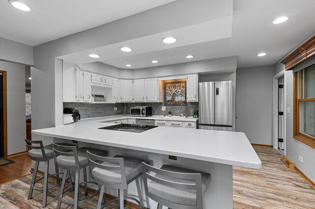 kitchen with stainless steel appliances, white cabinets, tasteful backsplash, light hardwood / wood-style floors, and kitchen peninsula