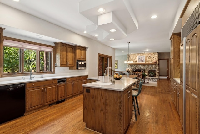 kitchen with a sink, light countertops, dishwasher, stainless steel microwave, and a center island with sink