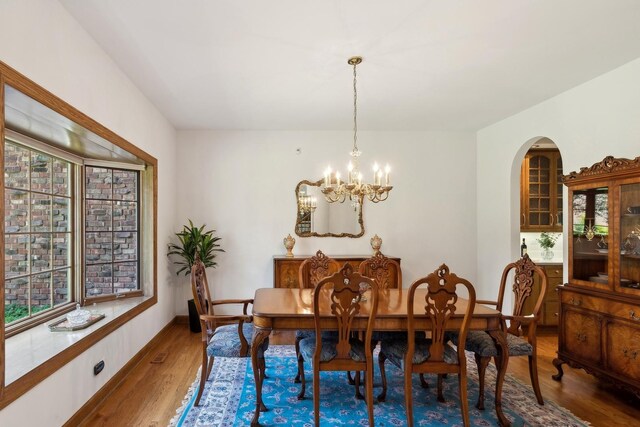 dining space with arched walkways, a healthy amount of sunlight, a notable chandelier, and wood finished floors