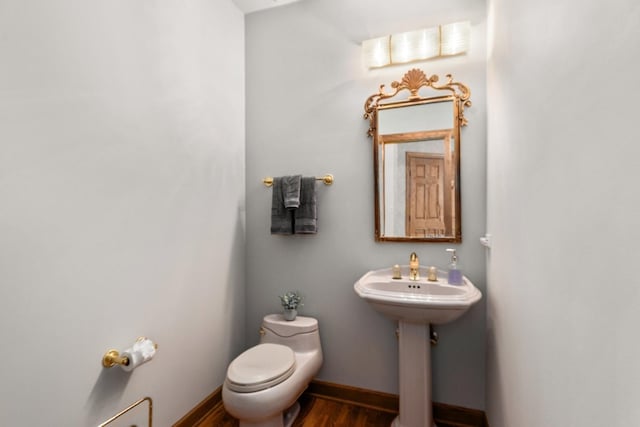 half bath featuring baseboards, a sink, toilet, and wood finished floors