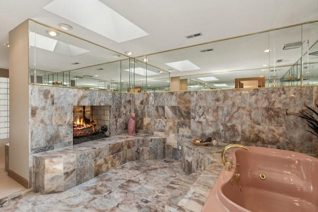 bathroom with a tub with jets, a skylight, a fireplace, and visible vents