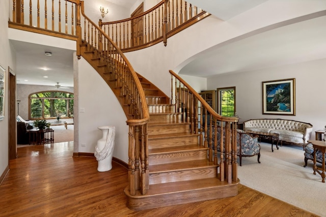 staircase featuring arched walkways, a towering ceiling, baseboards, and wood finished floors