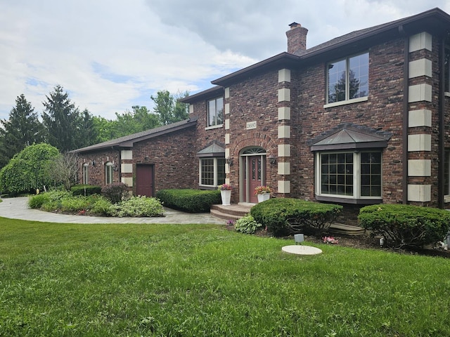 view of front of house featuring a chimney, a front lawn, and brick siding