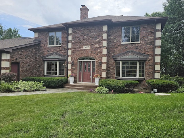 view of front of house with brick siding, a chimney, and a front yard