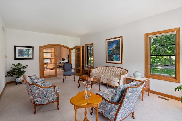 living area featuring arched walkways, french doors, light colored carpet, visible vents, and baseboards