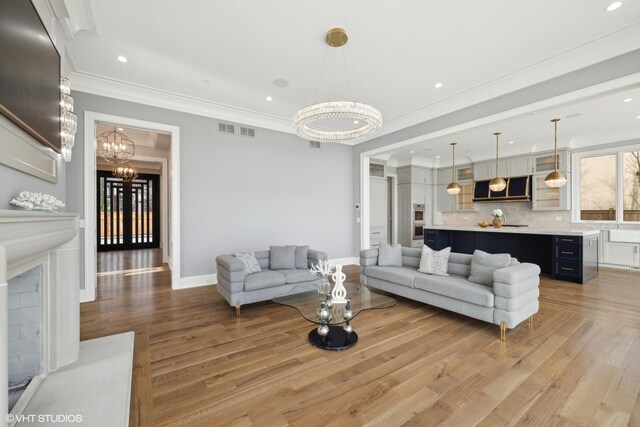 living room with light hardwood / wood-style flooring, a chandelier, a premium fireplace, and crown molding