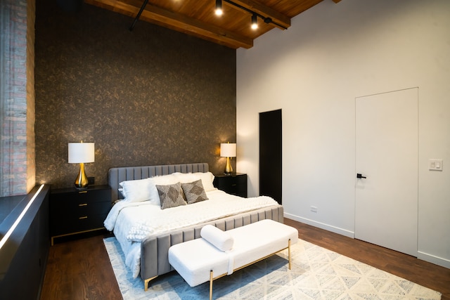 bedroom with beam ceiling, a towering ceiling, wood ceiling, and hardwood / wood-style flooring