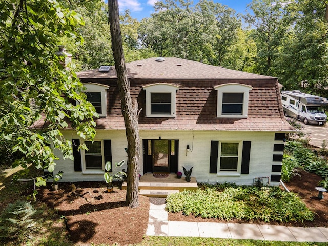 view of front of home featuring brick siding, mansard roof, and a shingled roof