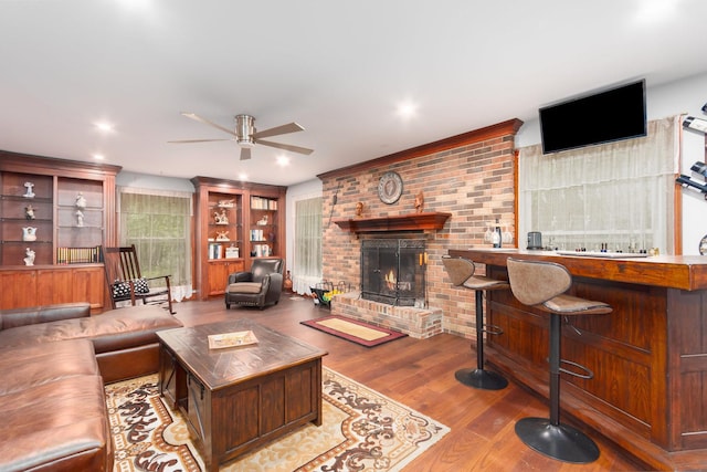 living room with light hardwood / wood-style floors, brick wall, ceiling fan, and a brick fireplace