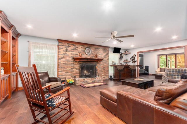 living room with ceiling fan, a fireplace, brick wall, and wood-type flooring