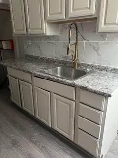 kitchen with backsplash, light stone counters, sink, and light wood-type flooring