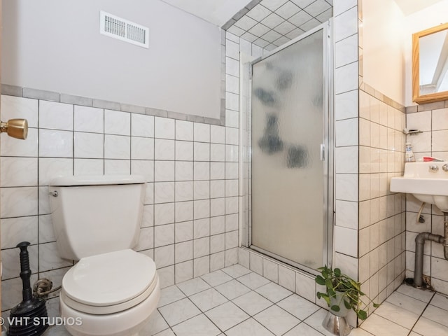 bathroom featuring a shower with shower door, toilet, tile patterned floors, and tile walls