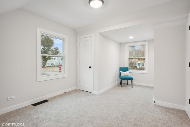 unfurnished room featuring a healthy amount of sunlight, lofted ceiling, and light carpet