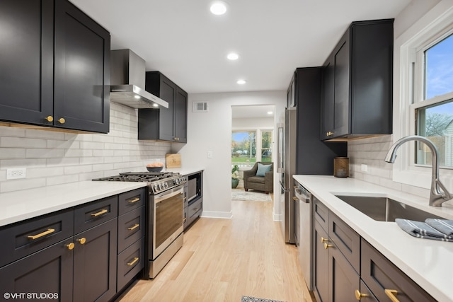 kitchen featuring appliances with stainless steel finishes, sink, a healthy amount of sunlight, and wall chimney range hood