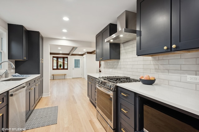 kitchen with appliances with stainless steel finishes, light wood-type flooring, light stone counters, wall chimney exhaust hood, and sink