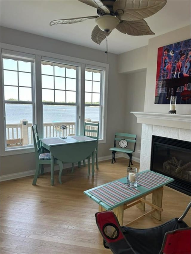 living room with a tile fireplace, light wood-type flooring, a water view, and ceiling fan