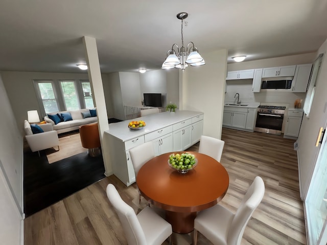 kitchen featuring stainless steel appliances, sink, an inviting chandelier, white cabinets, and light hardwood / wood-style floors