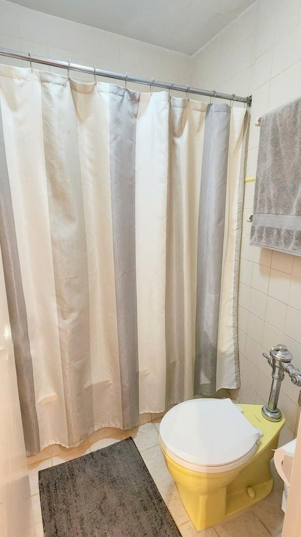 bathroom featuring toilet, tile patterned flooring, and tile walls