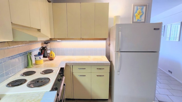 kitchen featuring tasteful backsplash, white refrigerator, range, cream cabinets, and light tile patterned floors