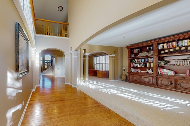 hallway featuring light hardwood / wood-style floors, decorative columns, and a high ceiling