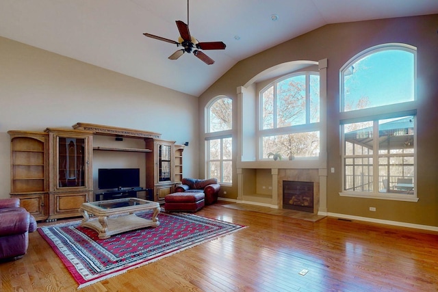 living room featuring high vaulted ceiling, light hardwood / wood-style floors, a tile fireplace, and ceiling fan