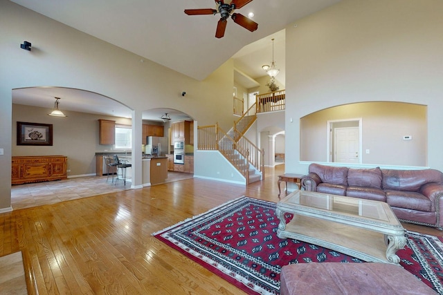 living room with ceiling fan, a high ceiling, and light wood-type flooring