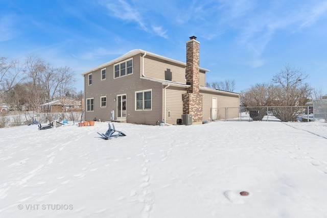 snow covered back of property with entry steps, a chimney, fence, and cooling unit